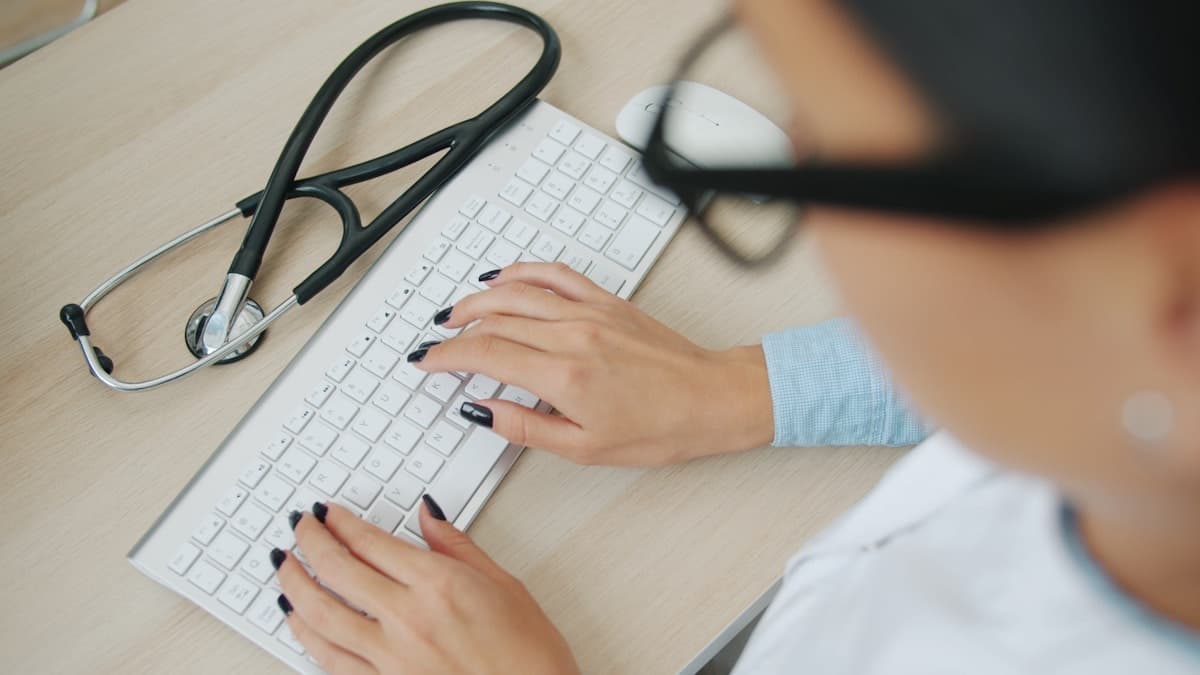 A doctor at a keyboard with a stethoscope nearby — telemedicine consultation